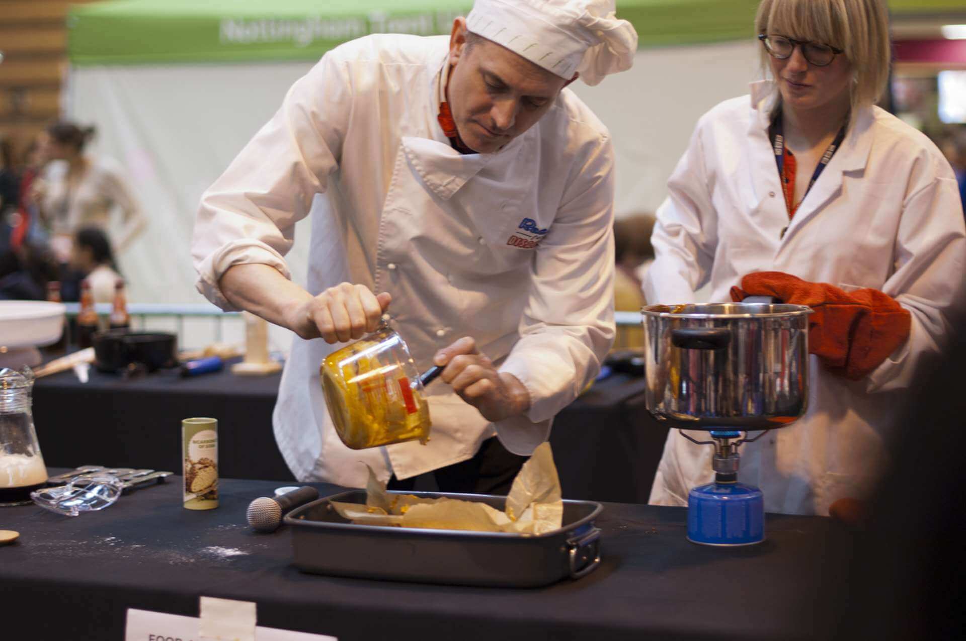 Dr Ken presents a BBC Food Sugar show at Big Bang Fair Dr Ken adds bicarbonate of soda to molten sugar to make homemade crunchie with aid of a BBC assistant.