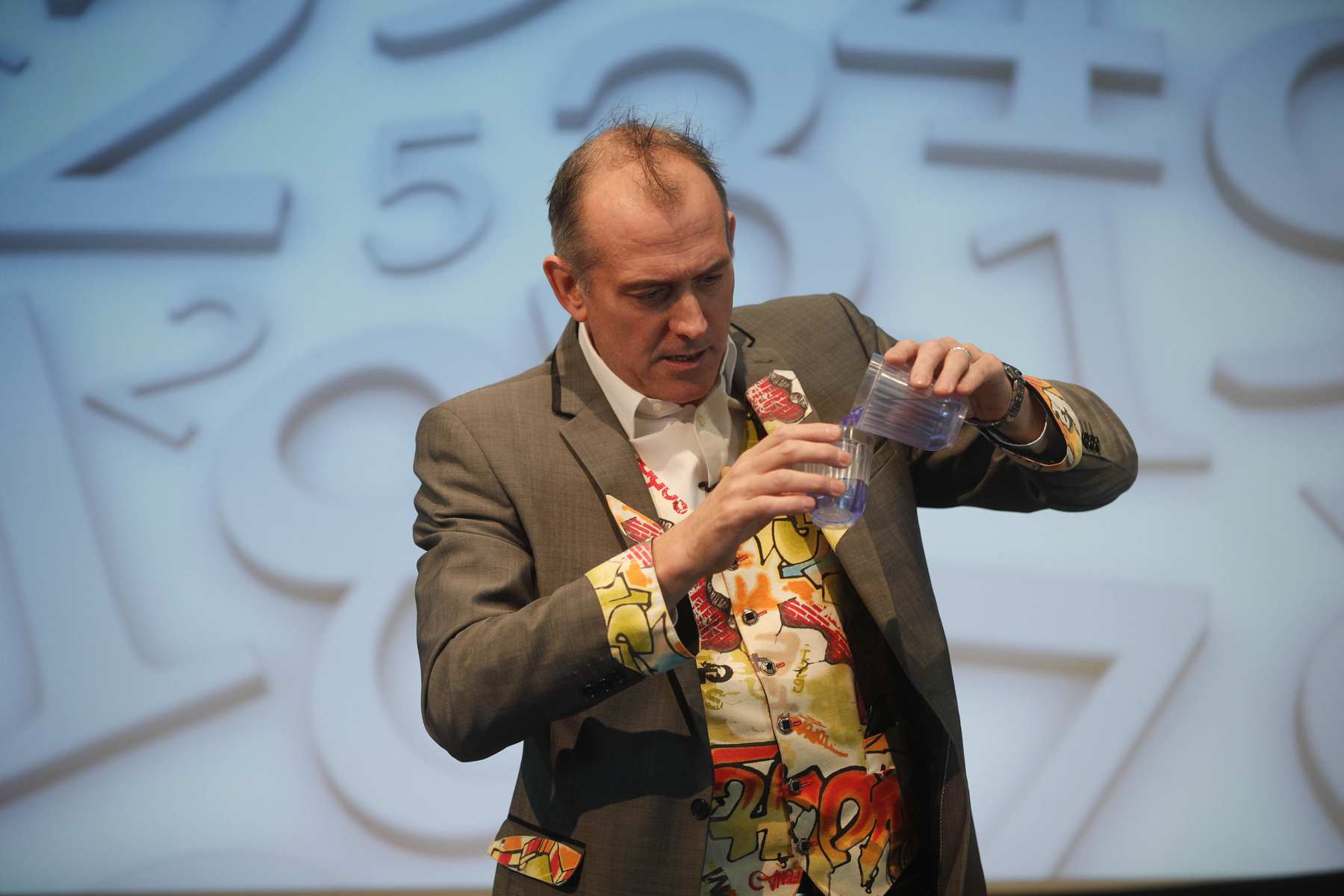 Volume Magic Dr Ken is pouring a blue liquid from a large container to a smaller one showing although they look different both have the same volume.