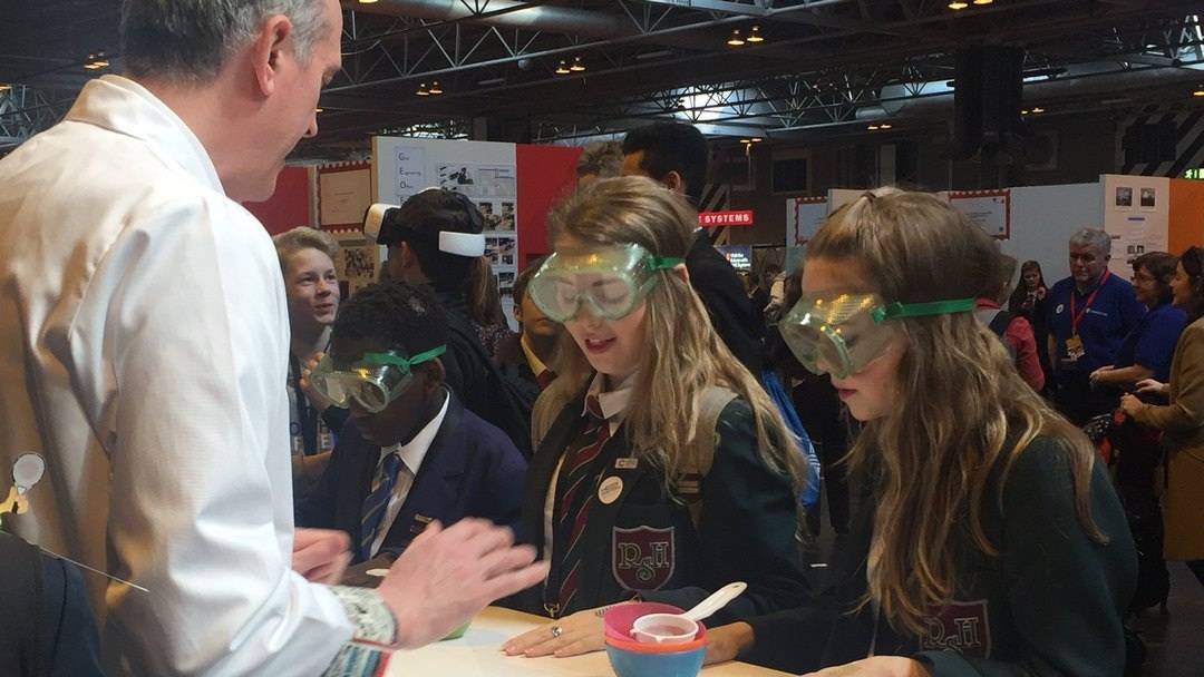 Three goggle wearing high school pupils get ready to race one another to separate a mixture of 3 different solids into 3 different plastic bowls using only a sieve and their hands.